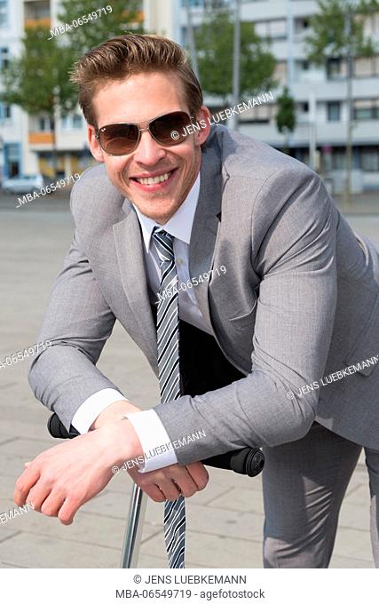 Man in grey suit with sunglasses and scooter, half portrait