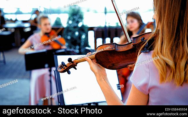 Little Group Of Violins In Pink Concert Dresses Plays Together On A Sunny Terrace. Focus On The Girl On The Right Back View