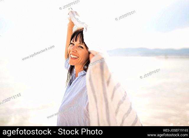 Cheerful woman holding scarf at beach