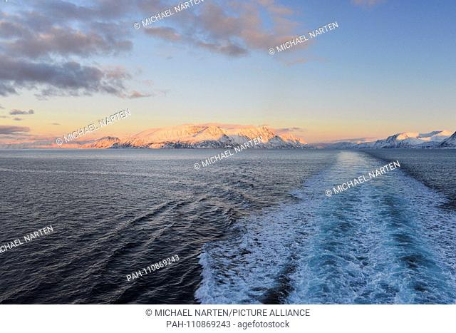 Foaming backwash in the Norwegian Sea with the snow-covered coastline from the island Sørøya and the Norwegian mainland in the distance in evening light