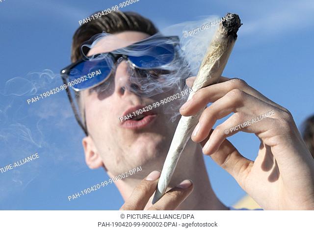 20 April 2019, Berlin: A young man from Berlin smokes an oversized joint for medical reasons during a protest action for legal cannabis use in Görlitzer Park