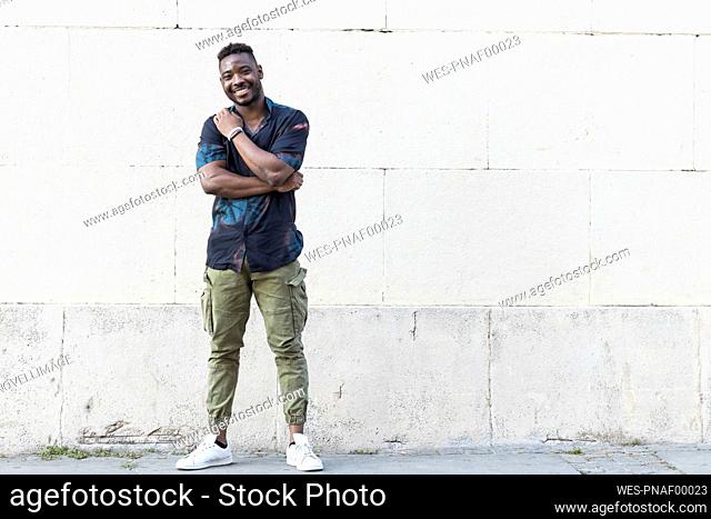 Smiling young man in casuals standing against white wall