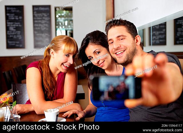 Lachende Gruppe macht Handyfotos von sich im Café