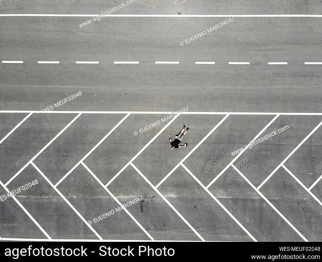Drone view of man lying on back in empty parking lot