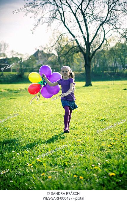 Little girl with balloons running on a meadow