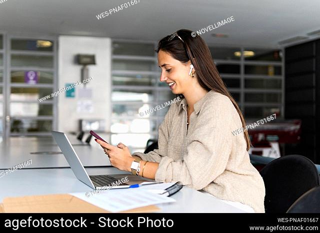 Smiling young businesswoman using smart phone at desk in office