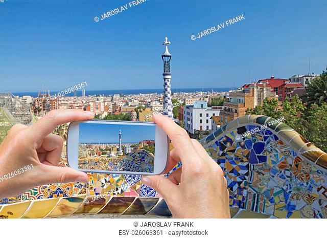 In the bottom left of the photo are hands holding smart phone and taking picture of the town of Barcelona (Catalunya, Spain)