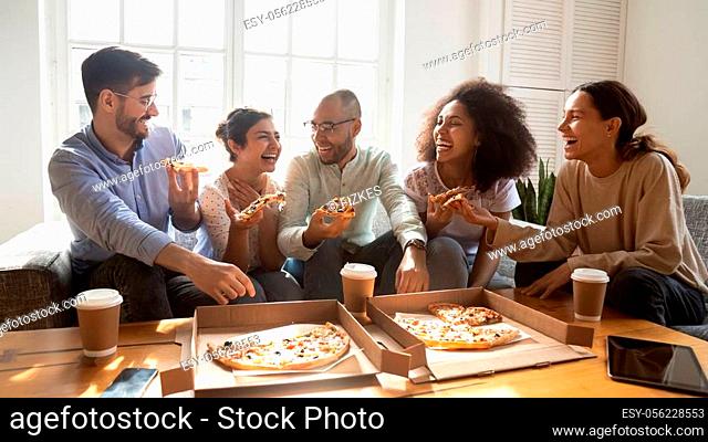 Overjoyed young diverse buddies eating ordered pizza for home party. Happy mixed race young friends enjoying spending free weekend time together, laughing