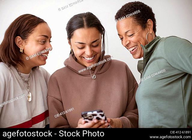 Happy mother and young adult daughters using smart phone