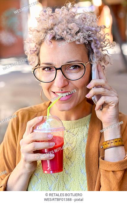 Portrait of a woman using smartphone and drinking a juice outdoors