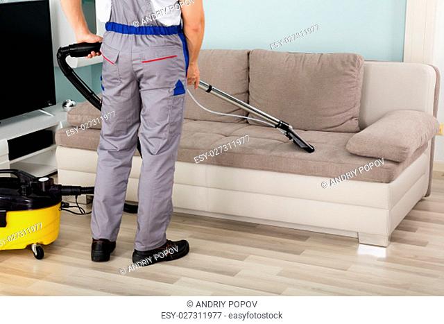Rear View Of Young Male Worker Cleaning Sofa With Vacuum Cleaner