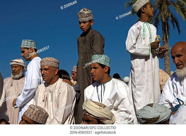 Gruppe omanischer Männer in Dishdash Nationaltracht auf dem Ziegenmarkt, Nizwa, Sultanat Oman / Group of Omani men in traditional Dishdash dress at the goat...