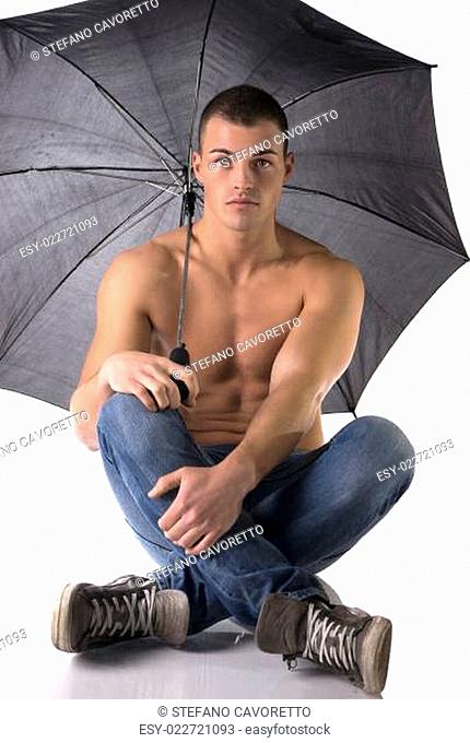 Shirtless young man on the floor under umbrella and looking at camera