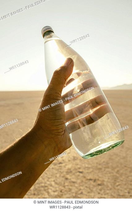 The landscape of the Black Rock Desert in Nevada. An essential element for survival. A man's hand holding a bottle of water. Filtered mineral water