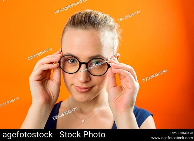 Young Caucasian woman with smiley face wearing glasses on orange background. Vintage style
