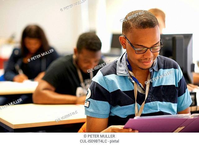 Male higher education student reading file in college classroom