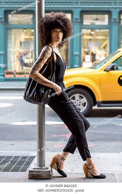 Fashionable woman leaning on pole in city