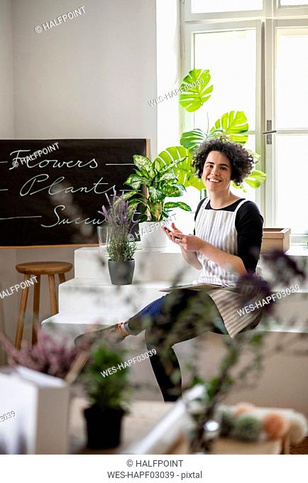 Portrait of smiling young woman using cell phone in a small shop with plants