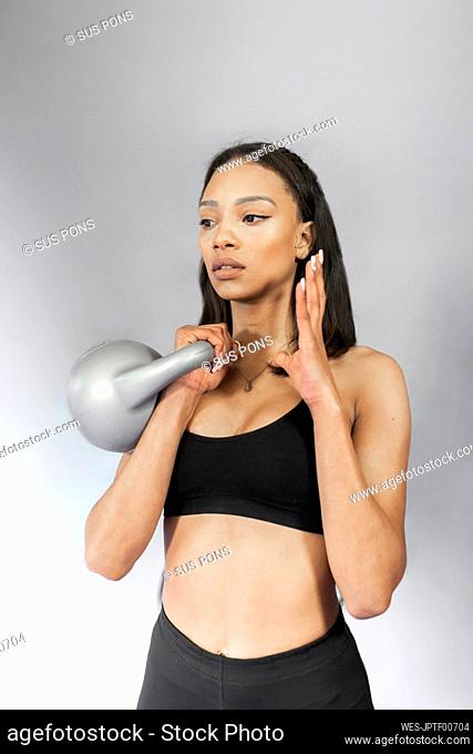 Slim young woman holding kettlebell standing in front of gray wall