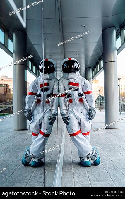 Male astronaut leaning on glass wall while standing on footpath