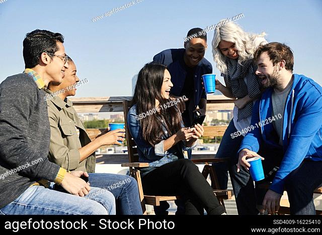 Group of young co-workers hanging out on rooftop patio laughing and having a drink
