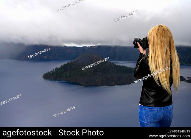 Long haired blonde holds her camera and photographing the extreme weather over Crater Lake, Oregon, United States of America
