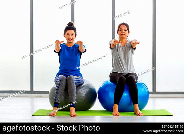Two Asian adult and young woman in sportswear doing aerobics yoga exercise with sitting on fitness ball indoor yoga studio