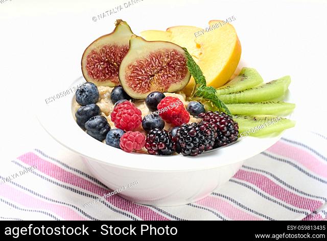 boiled oatmeal porridge with fruit in a round plate on a white table, healthy breakfast. View from above