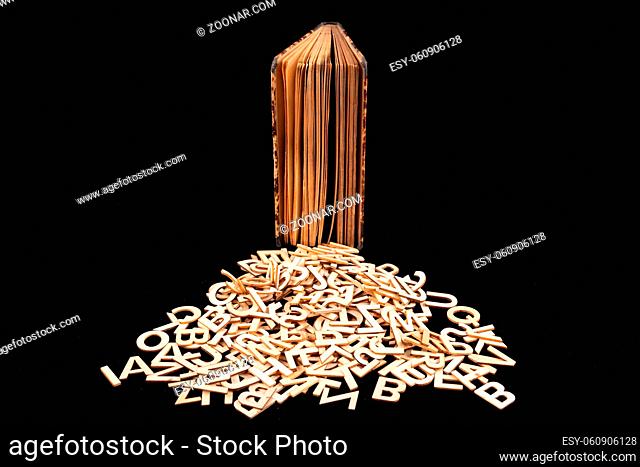 Old book and wooden letters. Wooden letters spilling out of the book. Dark background
