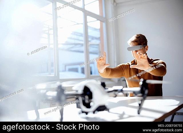 Businessman wearing virtual reality simulator making finger frame sitting with drone at desk