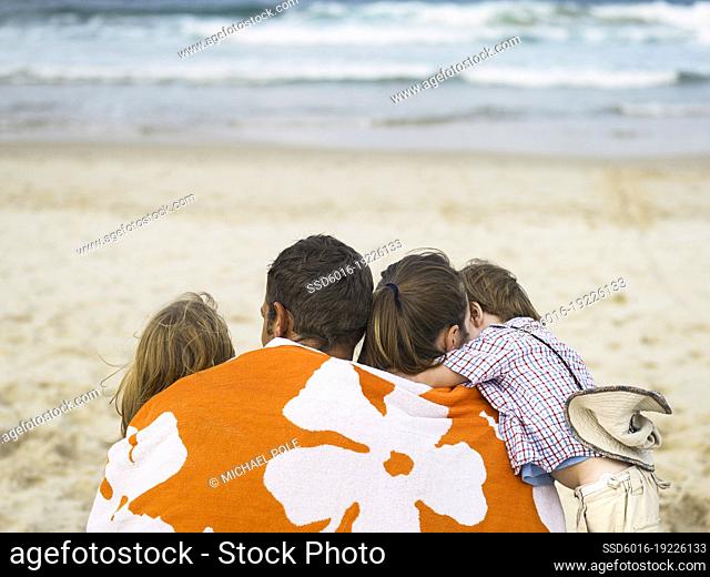 Family sitting at the beach with a towel wrapped around them