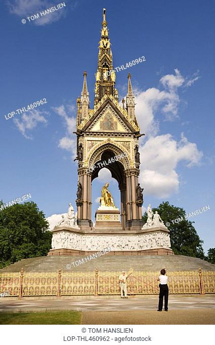 England, London, Hyde Park, A tourist standing for a photograph in front of the Albert Memorial in Hyde Park
