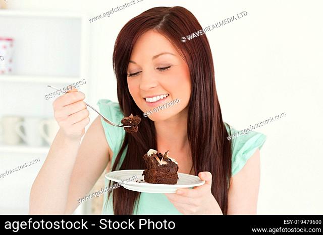 Smiling red-haired woman eating some cake in the kitchen