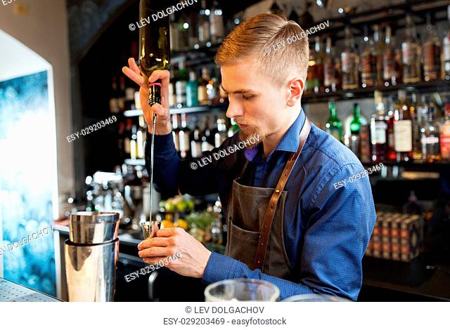 drinks, people and luxury concept - barman with shaker pouring alcohol from bottle into jigger and preparing cocktail at bar