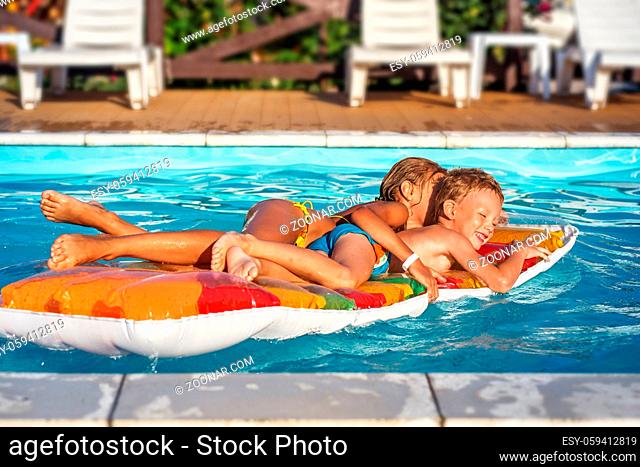 Little children on inflatable mattress in swim pool. Smiling kids playing and having fun in swimming pool with air mattress
