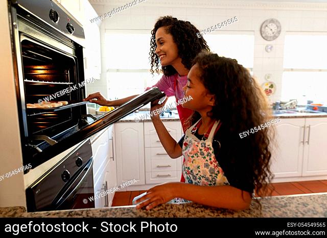 Side view of a mixed race woman in a kitchen with her young daughter at Christmas, looking into an oven