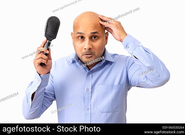 Portrait of a bald man touching his shaved head sadly while holding comb in his hand
