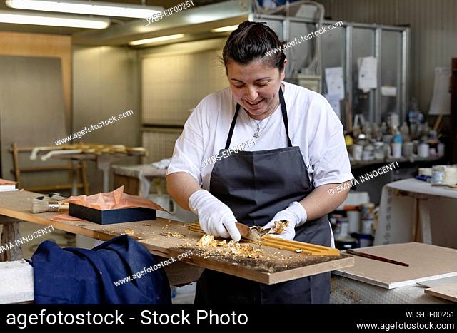 Expertise decorating frame with gold colored leaf while standing at workbench in workshop