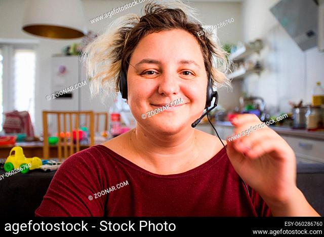 Portrait of cheerful young woman in headset while online conference call. Young mother working from home and raising kids