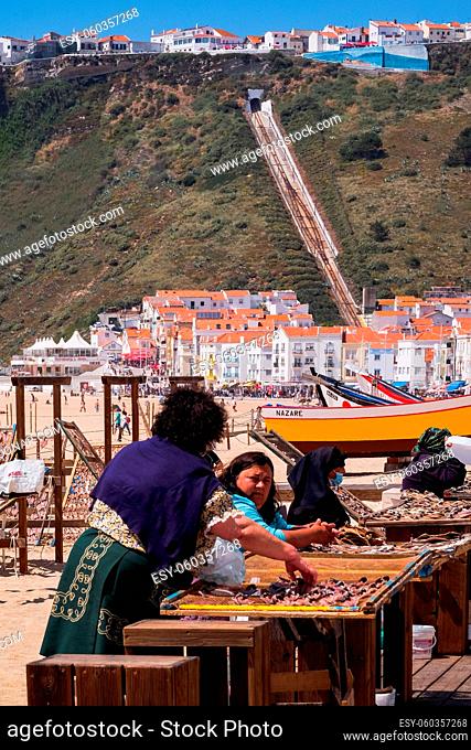 NAZARÉ, PORTUGAL - JUNE, 10 2020: Fishermen's Woman Selling Dry Fish in the Beach - Traditional Crafts in a Popular Resort in West Region