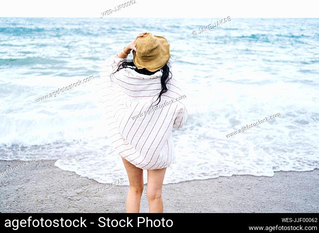 Woman wearing sun hat looking at sea on beach