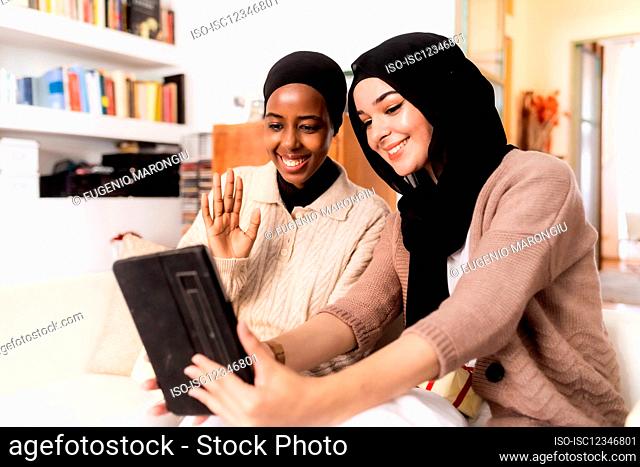 Two young women using digital tablet for video call