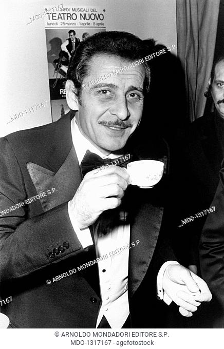 Domenico Modugno having a cup of coffee. Songwriter Domenico Modugno, dressed with a tuxedo, sips a coffee at Teatro Nuovo and smiles at the objective lens