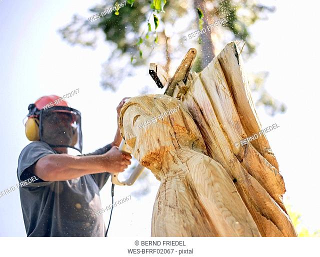 Wood carver carving angel sculpture, using chainsaw