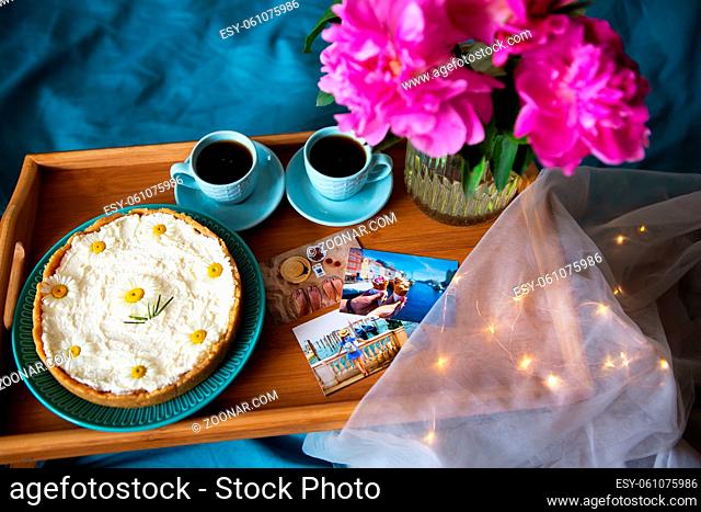 Coffee, pink peonies, cheesecake on a wooden tray, top view