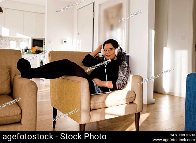 Smiling woman with down syndrome listening music while sitting on armchair at home