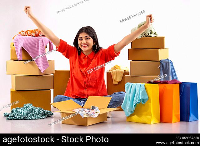 A young woman sitting amidst boxes, clothes and shoppingbags overjoyed on unpacking new dress