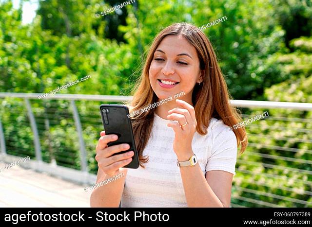 Beautiful young casual woman sending text message on mobile phone in city park
