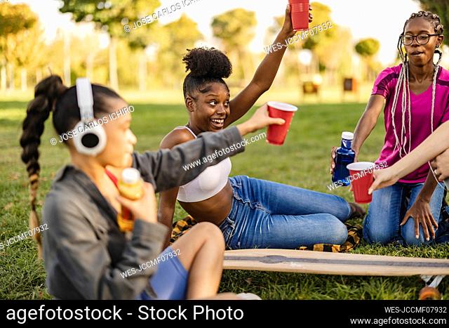 Happy woman with friends toasting drink at park