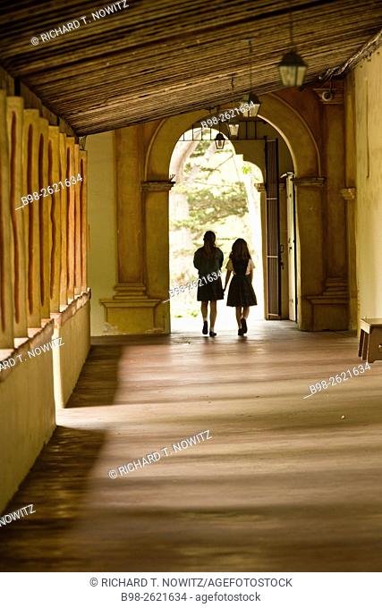 Two school girls walk down a hallway in the Mission San Carlos Borroméo del río Carmelo, also known as the Carmel Mission or Mission Carmel, Carmel-by-the-Sea